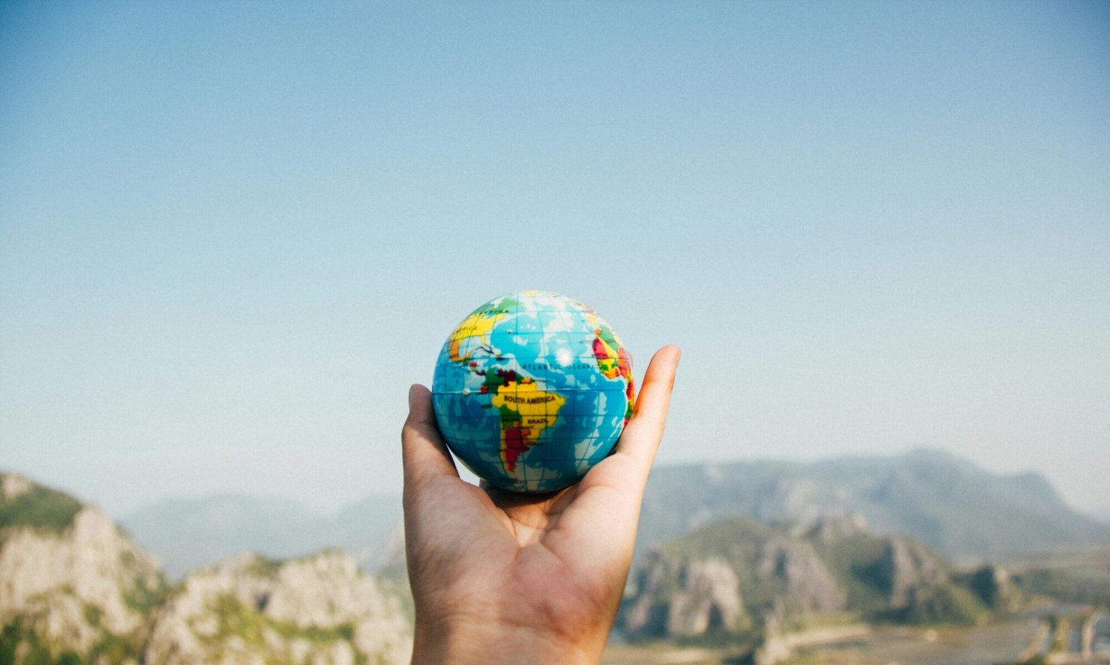 Hand holding a globe against a mountain background symbolizing travel and exploration.